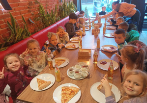 Cała grupa "Małpek" siedzi grzecznie przy stole i zajada pizzę.
