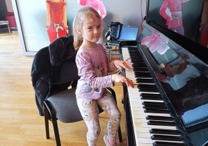 Dziewczynka siedzi przy pianinie i gra dla reszty rówieśników.