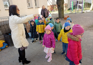 Pani Ewa wskazuje młodszym dzieciom miejsce poszukiwań czekoladowych jajeczek.
