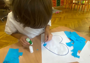 Chłopiec nakleja niebieski kawałek wydartego papieru w obrębie konturów serca.