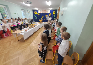 Dzieci w strojach galowych trzymają kolorowe chustki i śpiewają piosenkę pt. "Dzień Edukacji Narodowej".